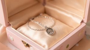 Boîte à bijoux élégante pour enfant, avec gourmette, petite médaille et chaîne disposées sur un fond satiné, ambiance douce et familiale, éclairage chaleureux.
